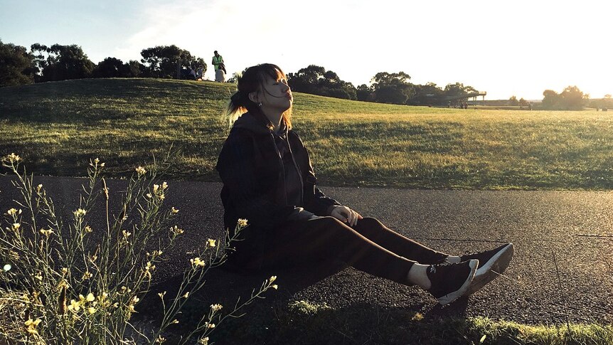 A young Chinese woman sits on the ground letting out a sigh.