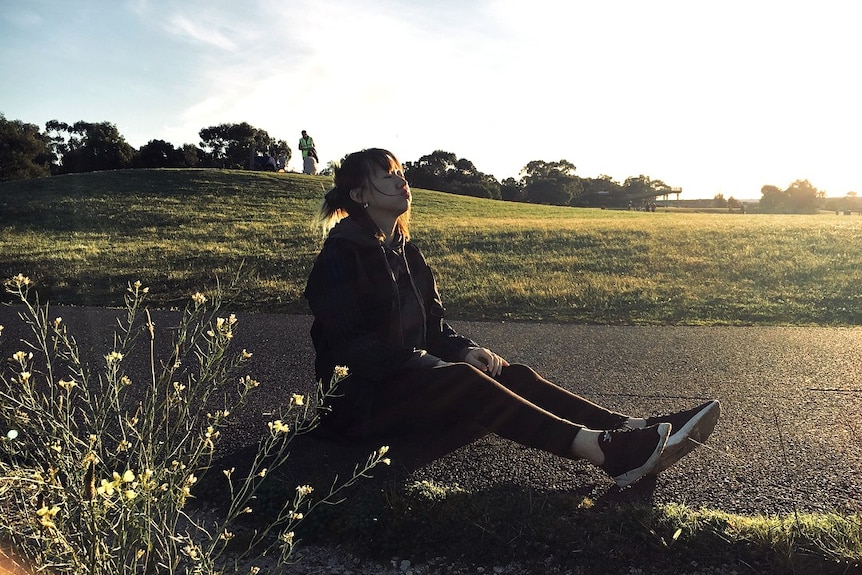 A young Chinese woman sits on the ground letting out a sigh.