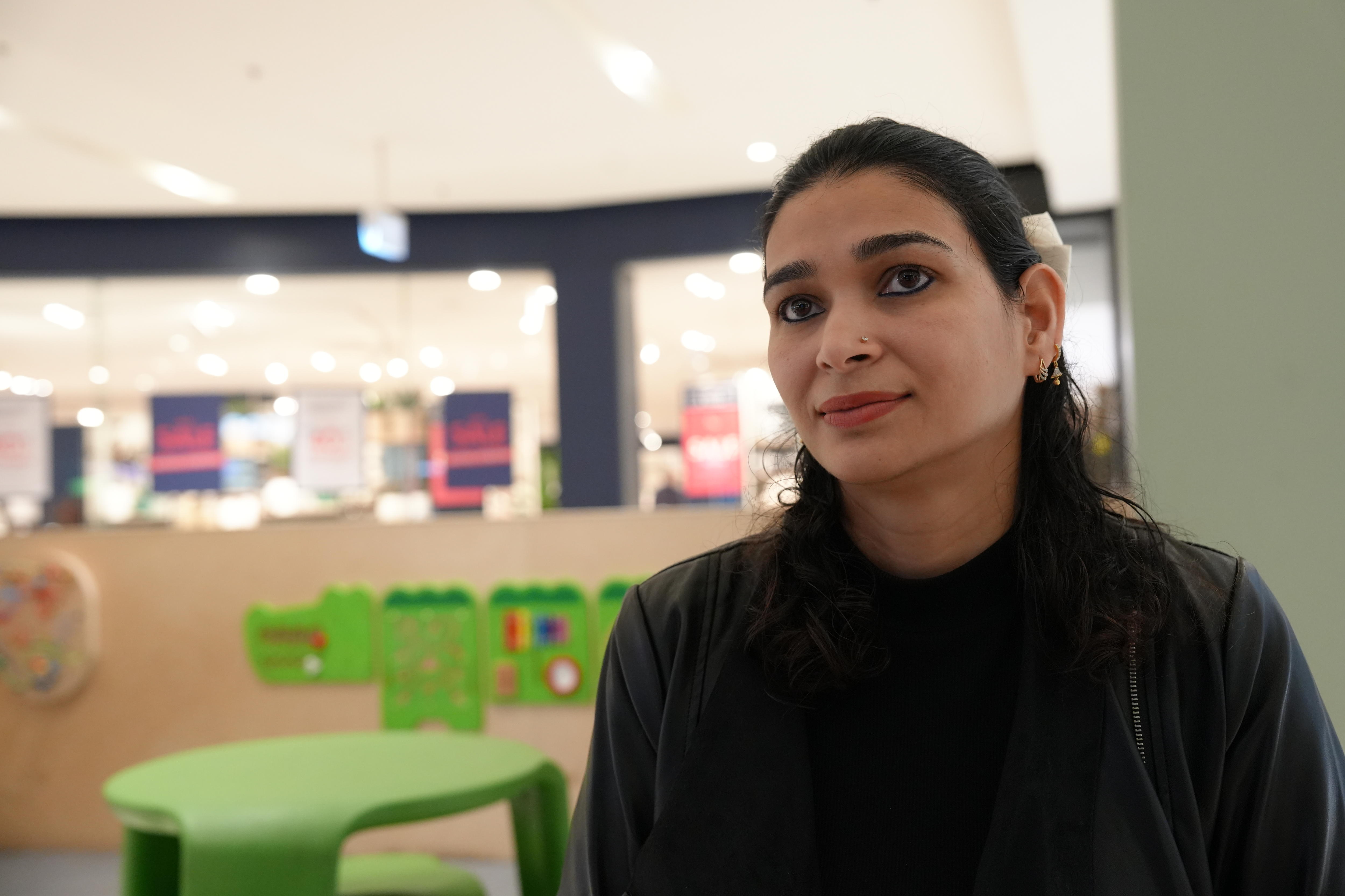 A woman with long, dark hair sits at a table in a shopping complex.