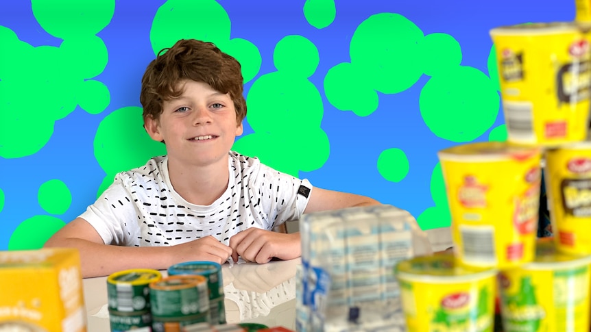 Ashton smiles while sitting at a table full of various packaged food items.