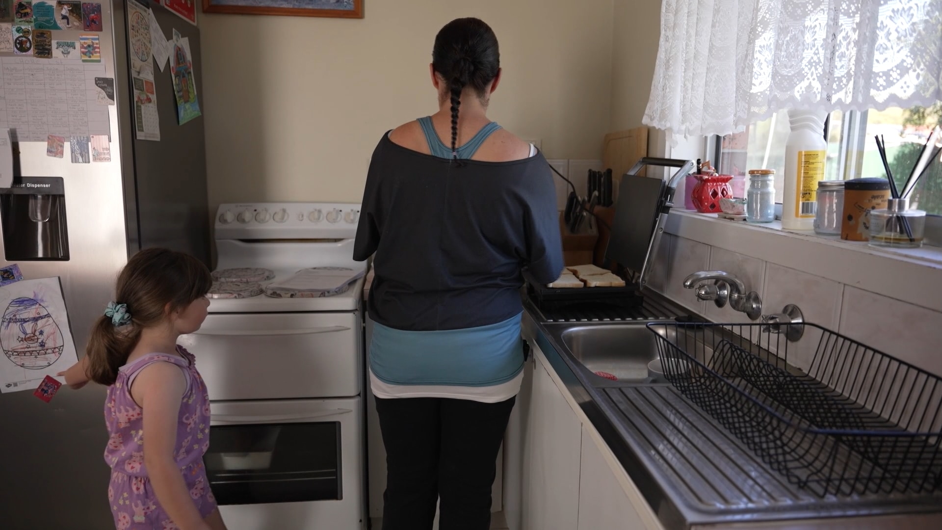 Dana Wing stands in her kitchen with her back to the camera as her daughter stands side on to the camera.