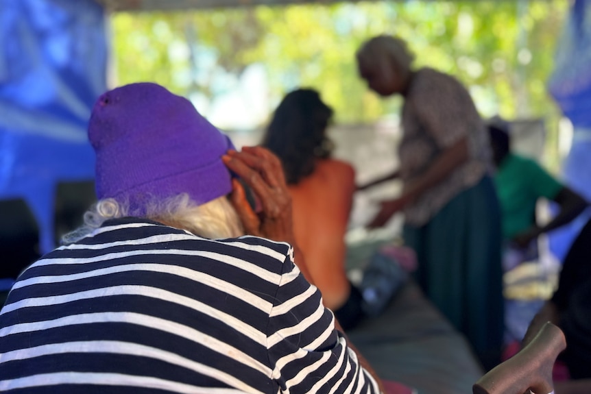 An elderly Aboriginal woman facing women healing a younger woman.