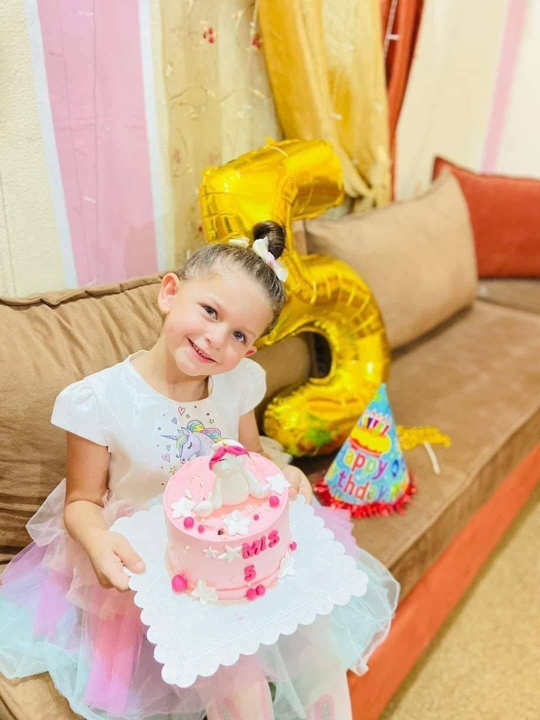 Tamim's daughter smiles on a couch with a number 5 birthday balloon behind her.