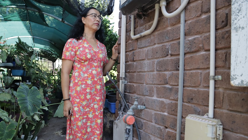A burnt out solar panel inverter on a wall, with a woman standing next to it.
