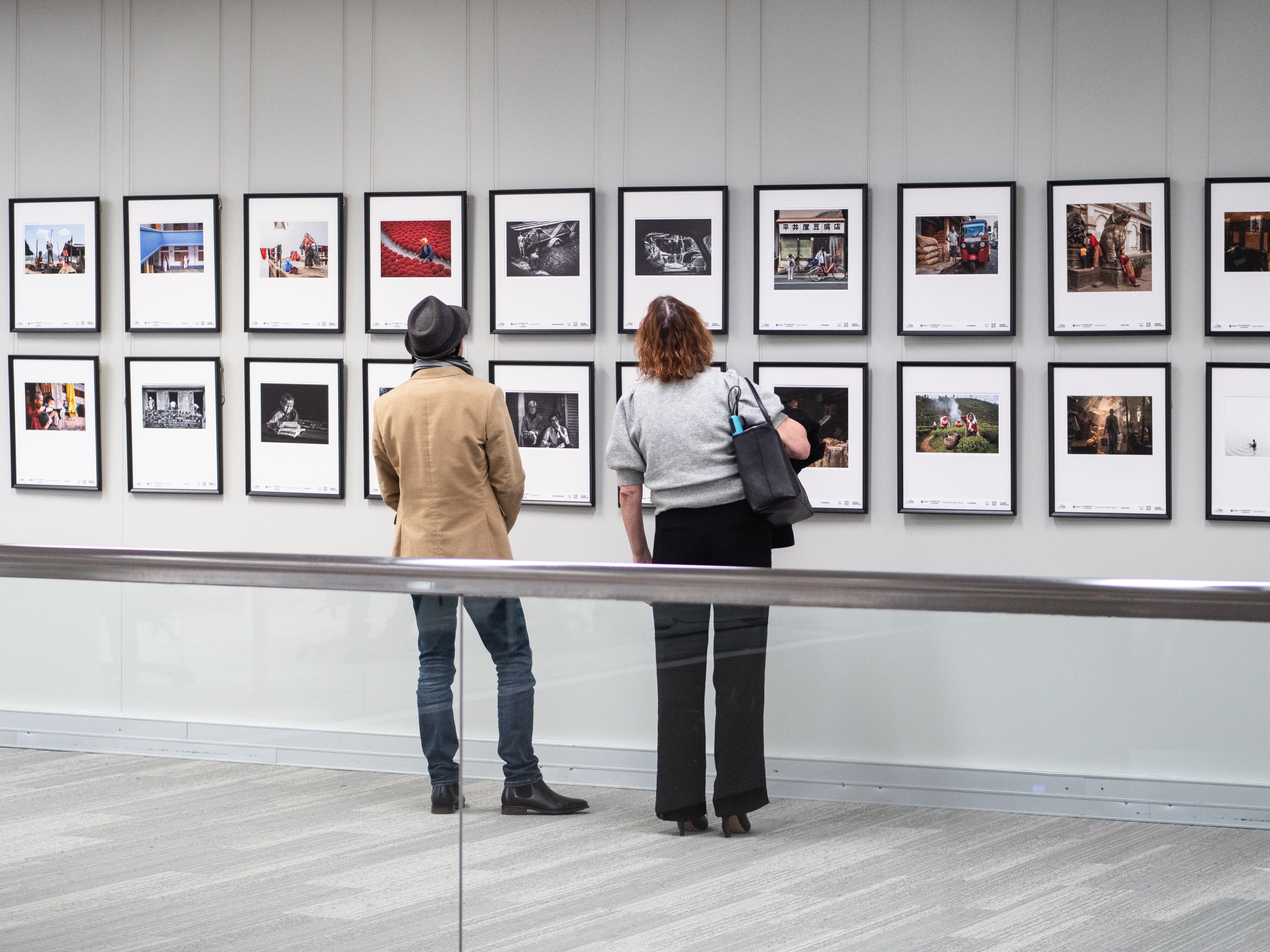 Two people look at many framed photographs on a wall.