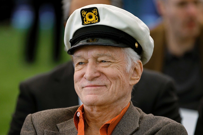 Playboy founder Hugh Hefner wears a boat captain's hat while smiling.