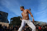 An Indigenous man dances at Federation Square while a crowd watches on.