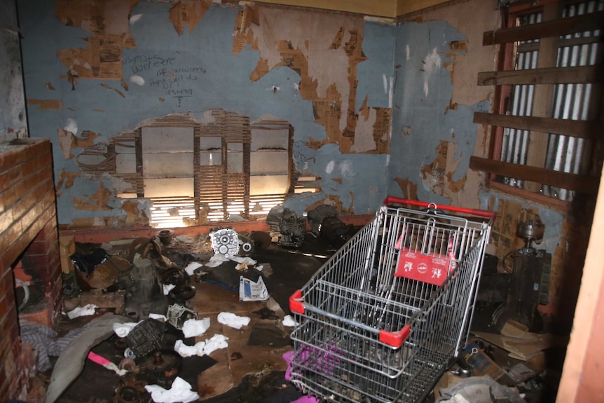 Room in derelict house with rubbish and shopping trolley.