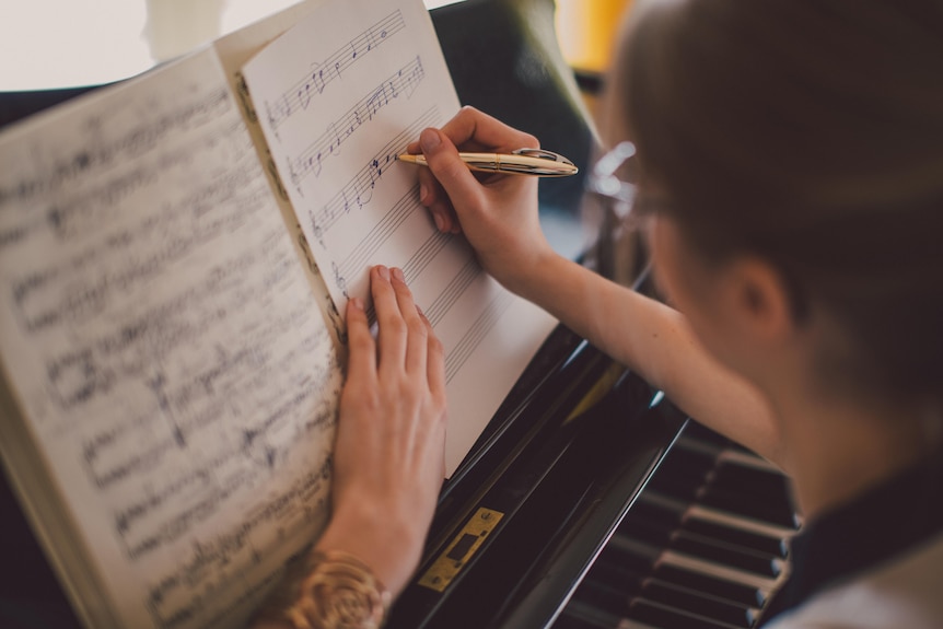 Man writing music on a sheet at a piano 