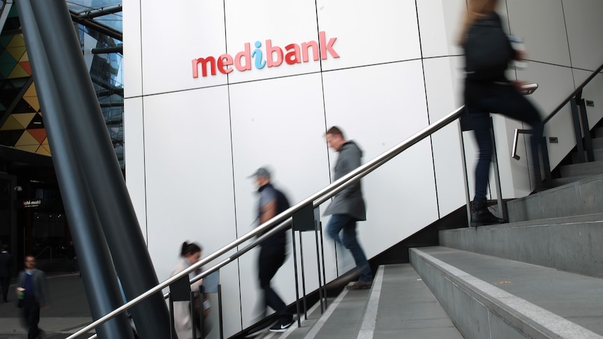 A few people walk up and down stairs. The left wall is white paneling bearing the Medibank logo