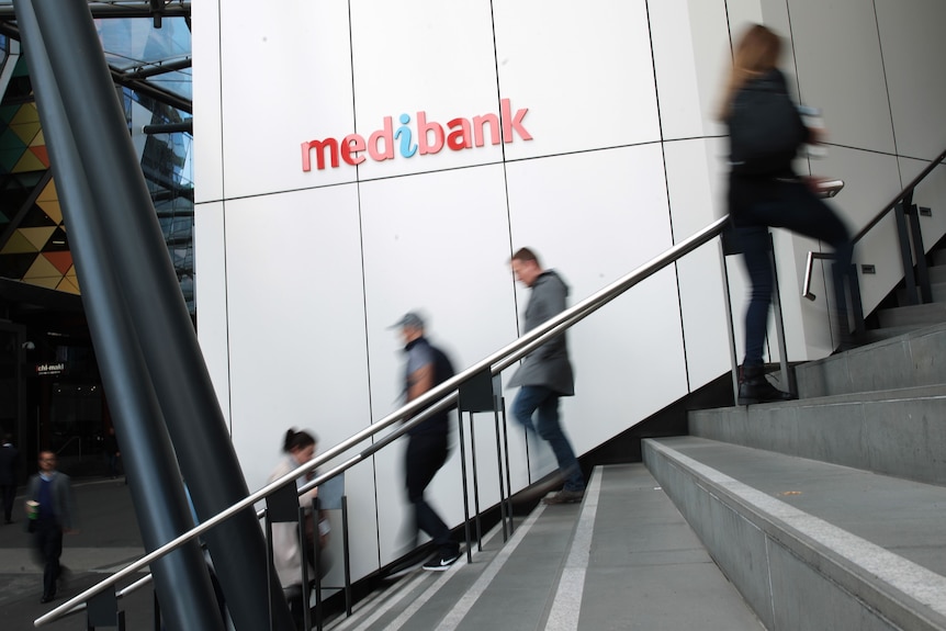 A few people walk up and down stairs. The left wall is white paneling bearing the Medibank logo