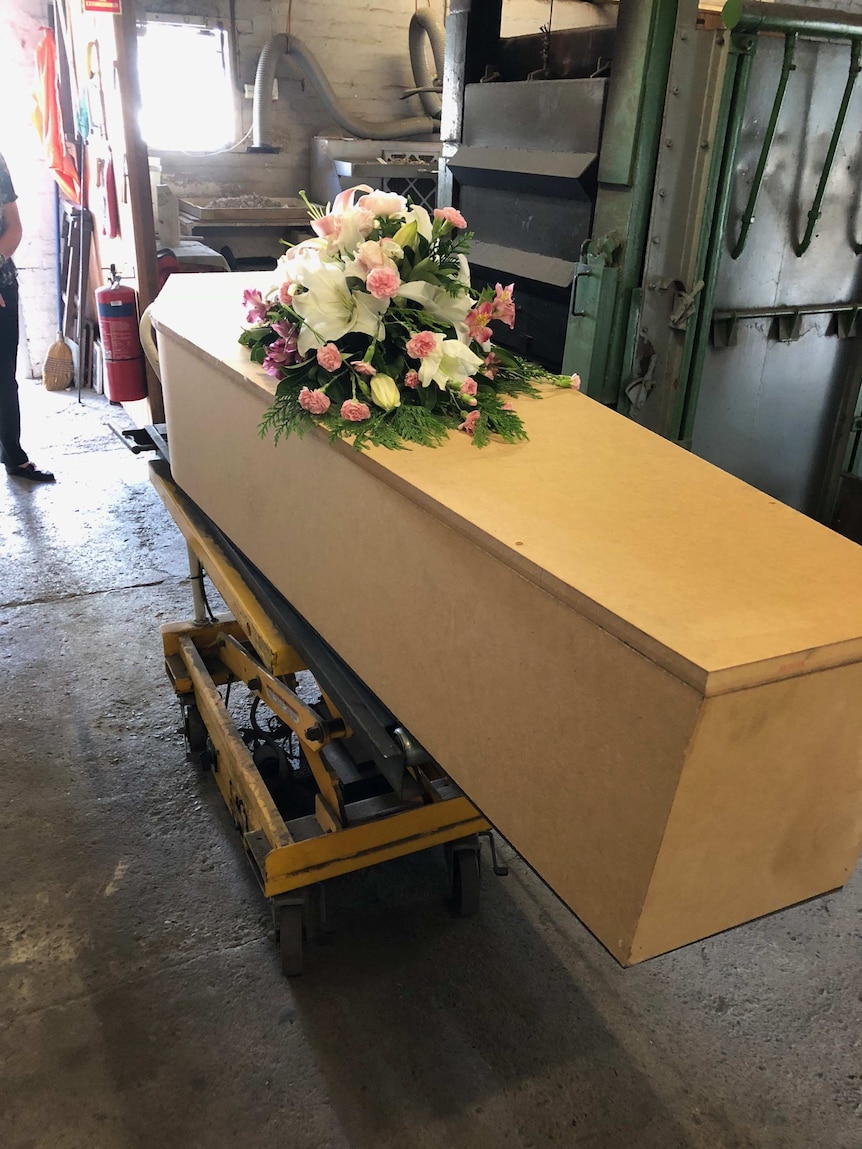 A pine or woodchip casket with a bouquet on top.