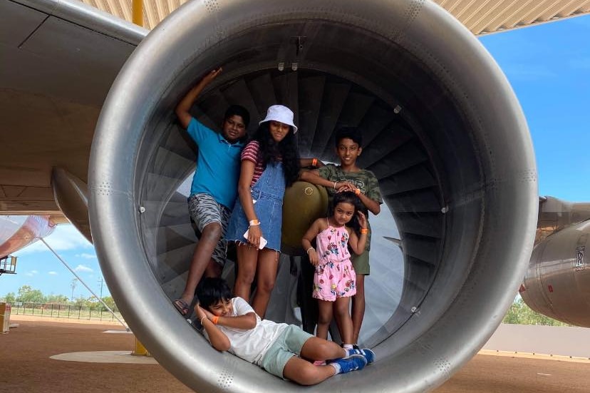 Five kids pose for a photo standing in the turbine engine of a plane at the Qantas Founders Museum.