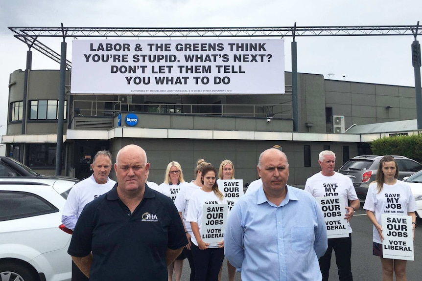 People stand in a hotel car park under a large sign.