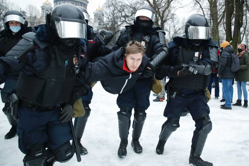 A man is carried by a group of police officers in shiny helmets.