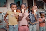 Four children lick vanilla ice creams outside a shop in Madagascar. Three look into the camera as they enjoy treat.
