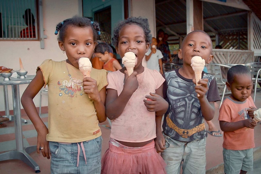 Four children lick vanilla ice creams outside a shop in Madagascar. Three look into the camera as they enjoy treat.