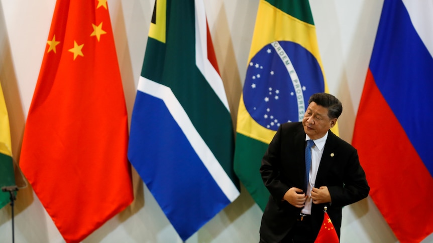 President Xi stands up in front of Chinese, South African, Brazilian and Russian flags. 