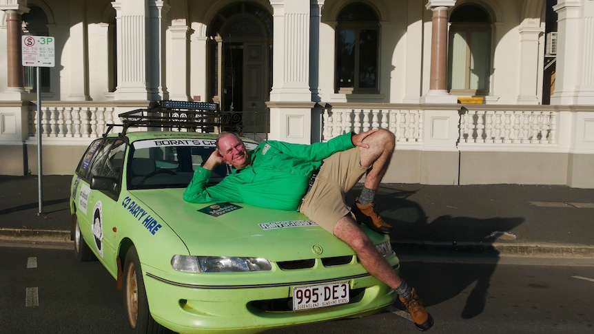 A man lies on the bonnet of a brightly coloured station wagon.