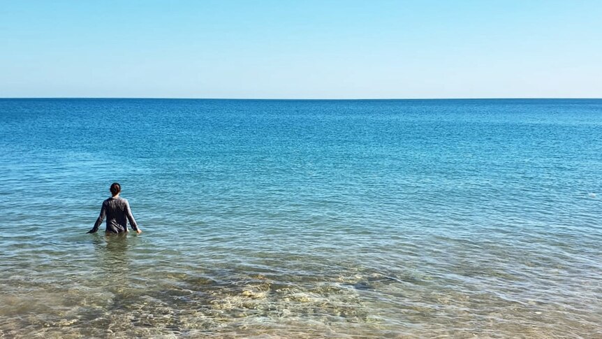 A woman stands in the water of a flat sea.