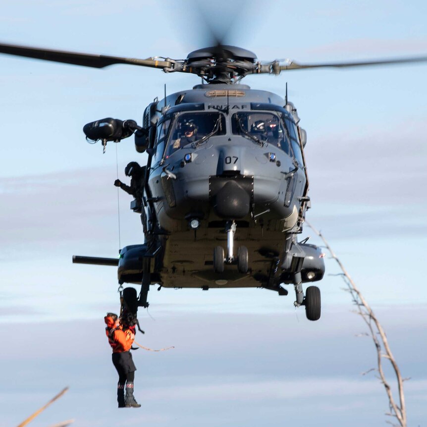A helicopter hoists a search rescue worker aboard during a rescue.