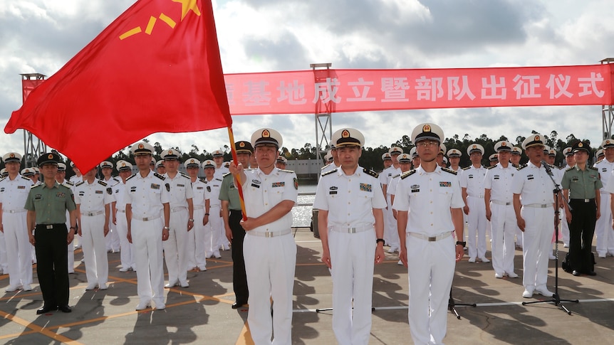 A formation of Chinese naval officers in dress whites holding a Chinese flag