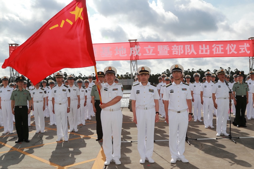 A formation of Chinese naval officers in dress whites holding a Chinese flag