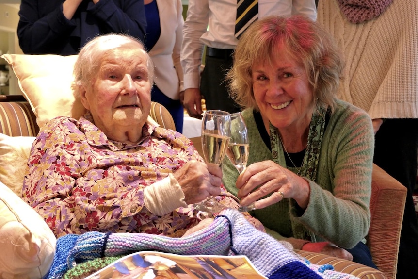 An elderly woman shares a glass of champagne with another woman.