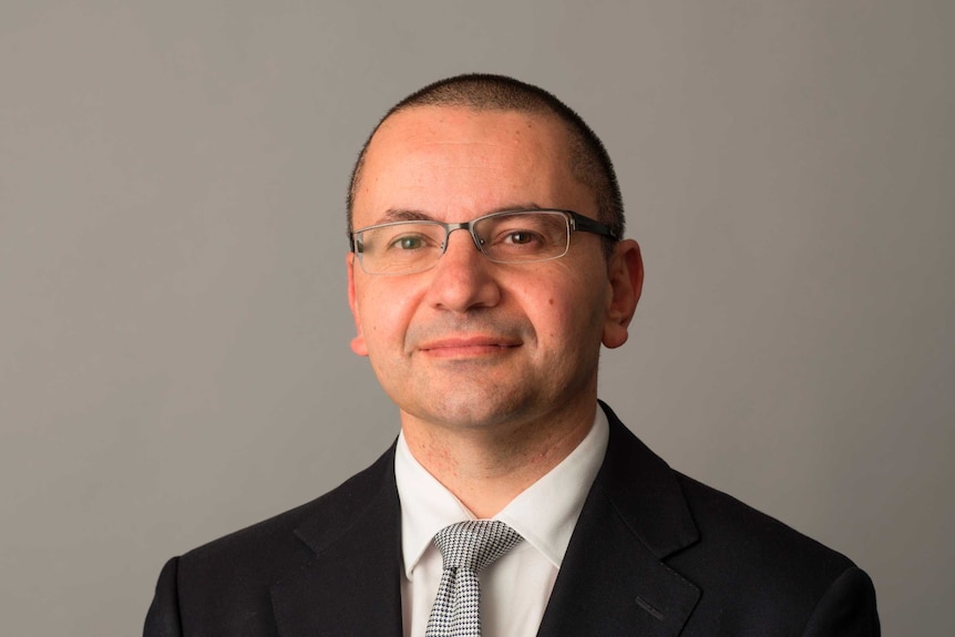 Professional headshot of a man with a shaved head and glasses wearing a suit.