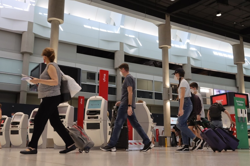 Wide shot of travelers in masks walking through the Brisbane Airport departure terminal.