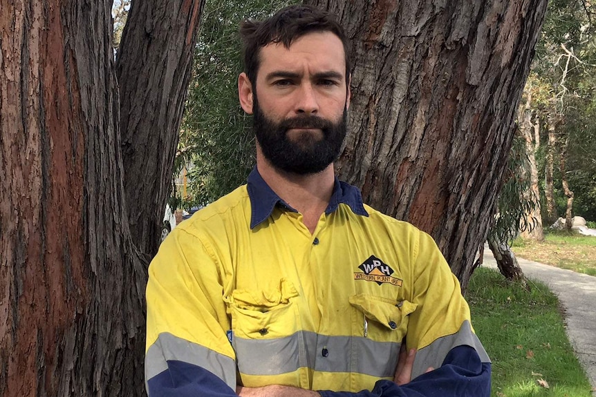 Matthew Ryan stands, arms folded across his chest, wearing work gear.