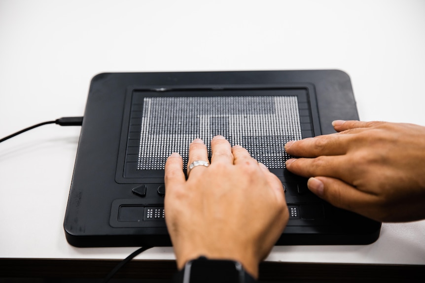 A close up of a black rectangle device with a screen on it, hands touching the screen.