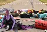 A woman painted purple looks to the sky surrounded by other people laying on a road.