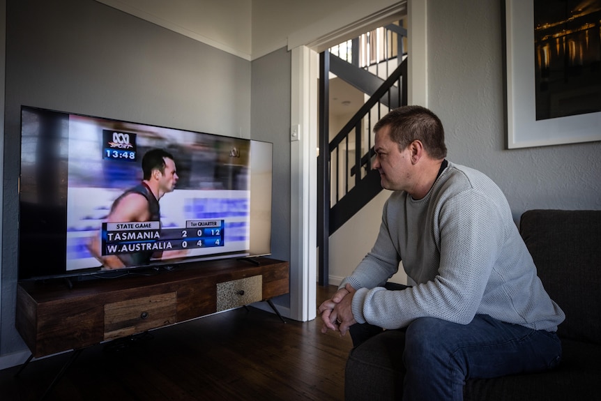 A man sits on a couch watching an old football game.