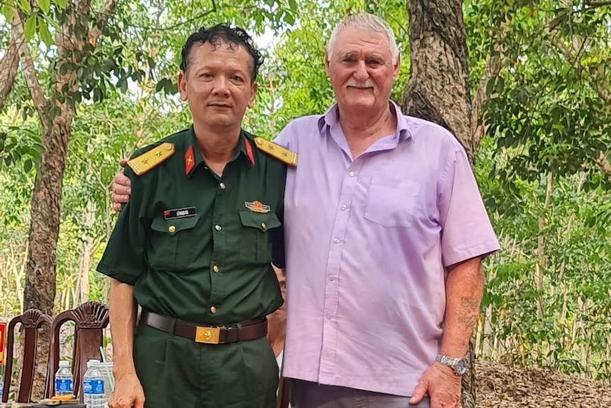Vietnamese soldier in uniform of the left with John Bryant on teh right. They are standing in the jungle in front of trees. 