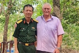 Vietnamese soldier in uniform of the left with John Bryant on teh right. They are standing in the jungle in front of trees. 
