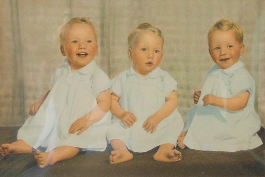 Three baby boys all dressed in matching gowns.