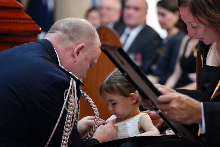 A man pins a medal to the dress of a young girl.