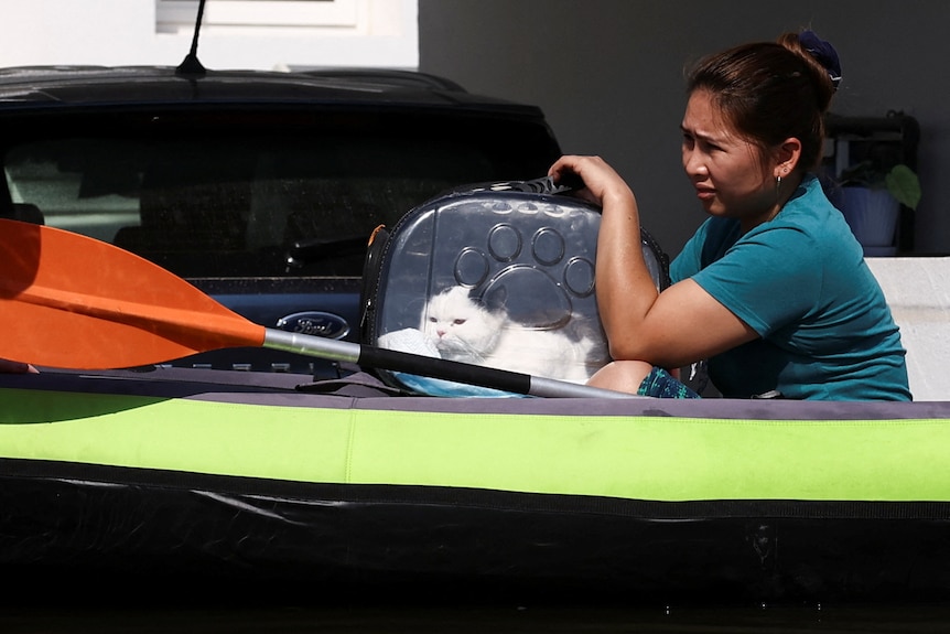 A woman canoes through flodwater with a cat in a carrier.
