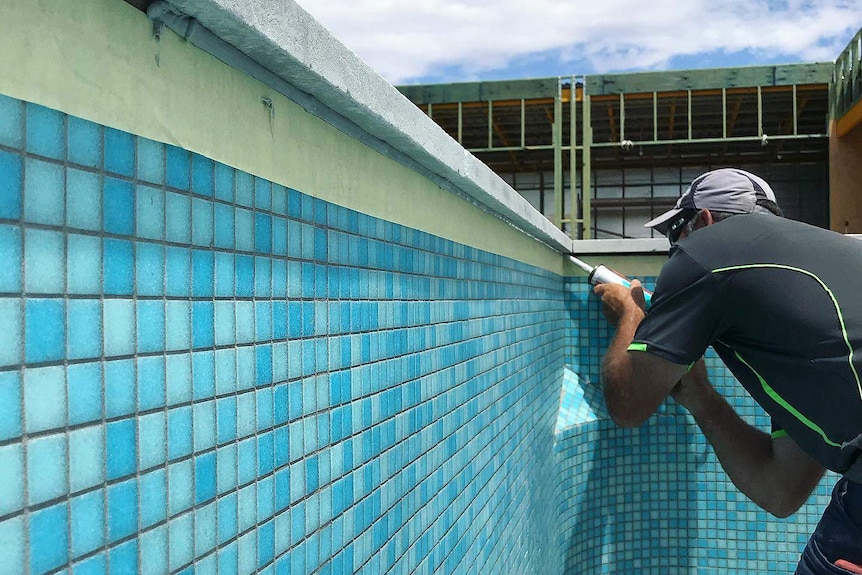 A man standing in a blue tiled pool using sealer to watertight the pool edges