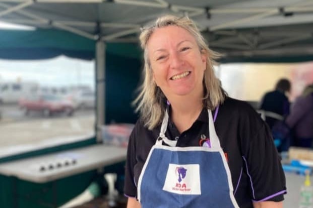 A smiling woman with blonde hair wearing a blue apron