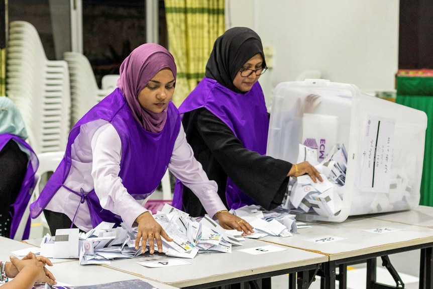 Two women sort through ballot papers on a table. 