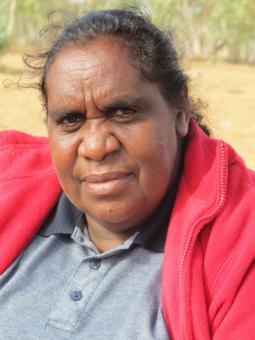 April is outside in the sun. She isn't smiling, but she looks happy and friendly. She is wearing a red top.