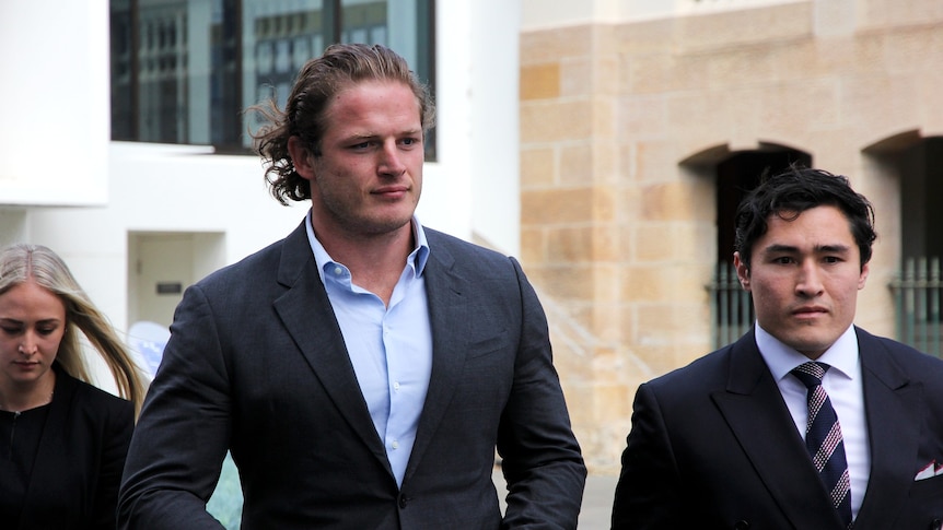 Two men in dark suits walk towards a courthouse.