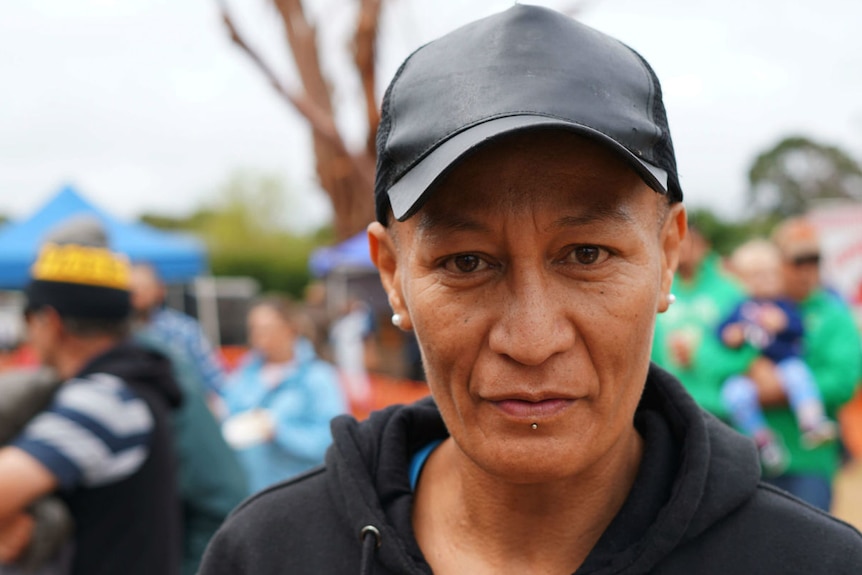 A woman wearing a cap looks into the camera with blurry crowds behind her.