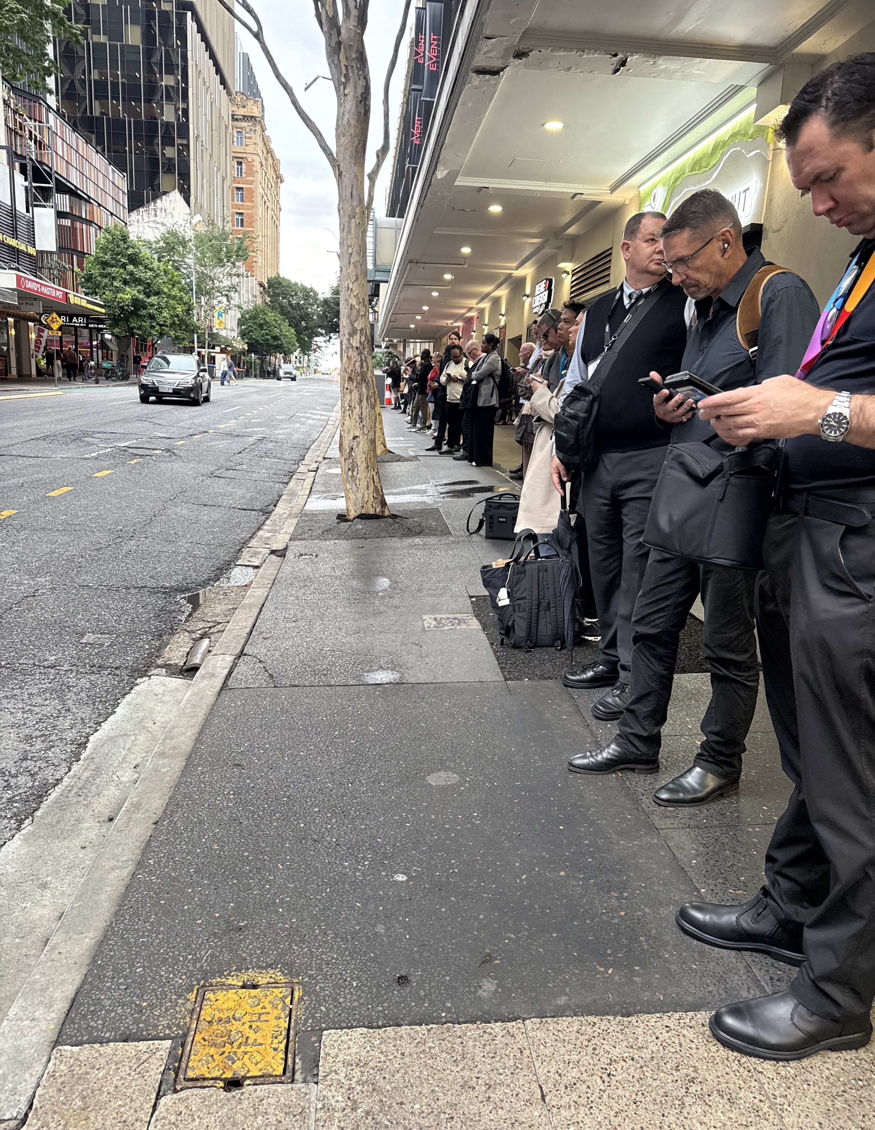 A queue of people waiting down a street for a bus. 
