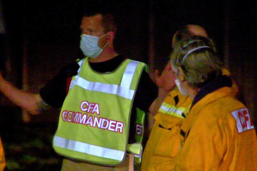A man wearing a CFA commander bib briefs other CFA staff at night.