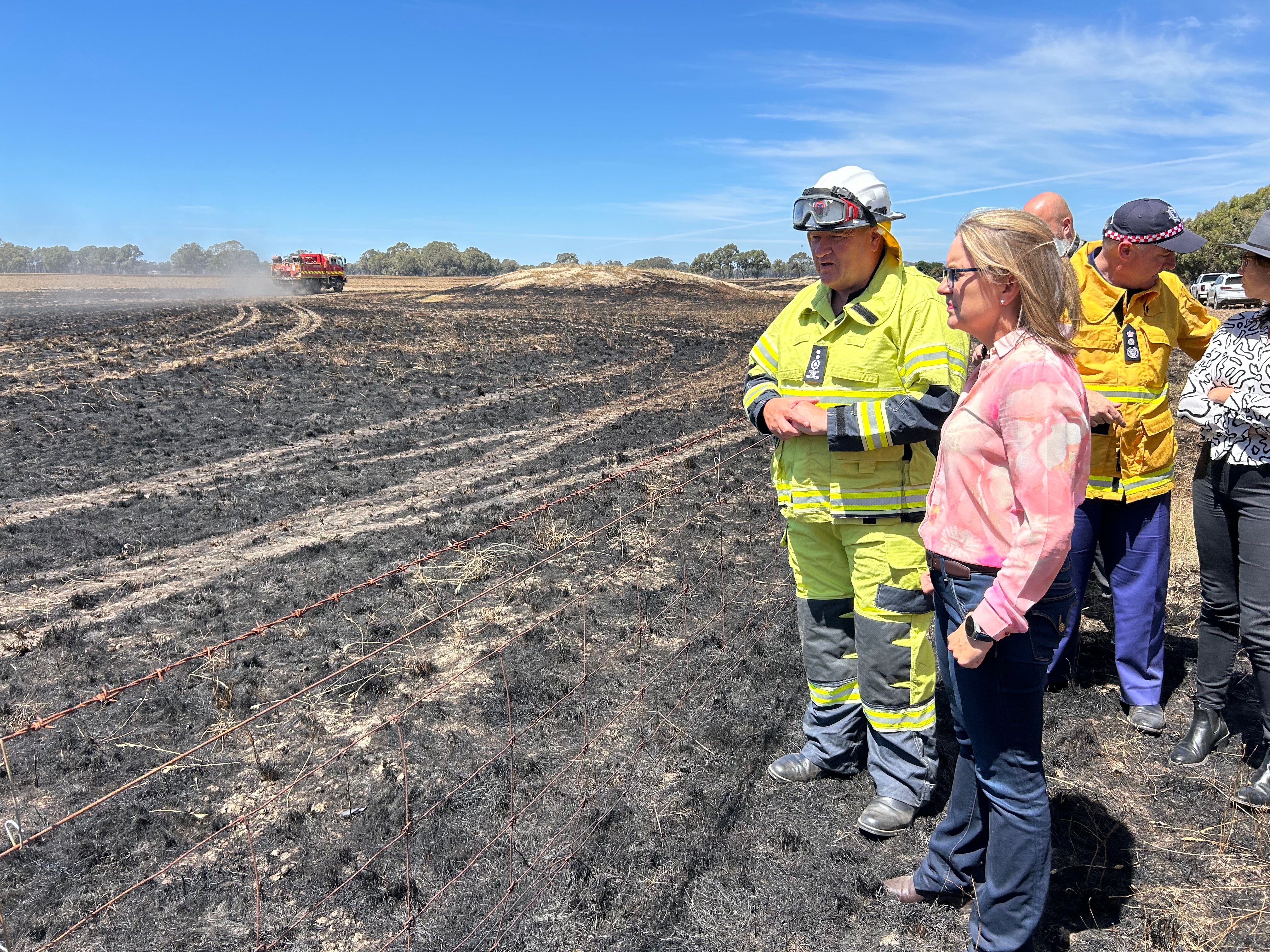 Victorian Premier Jacinta Allan standing on a burnt out field with firefighter.