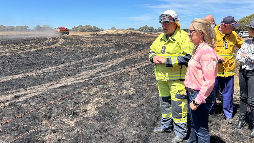 Victorian Premier Jacinta Allan standing on a burnt out field with firefighter.
