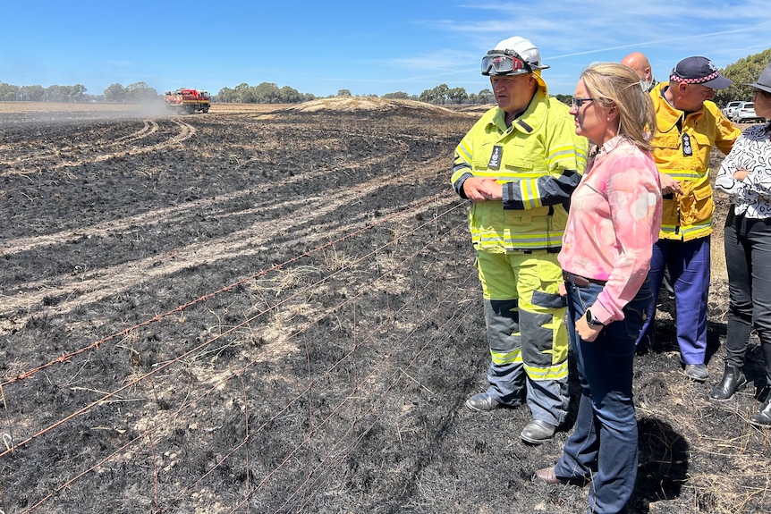 Victorian Premier Jacinta Allan standing on a burnt out field with firefighter.